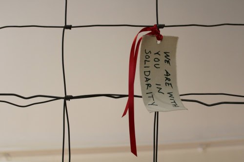 Messages of Hope and  Resistance, detail,  2025, Metal, fence, rocks, cement, canvas, ribbon, ink, and wire,  72 by 96 by 12 inches