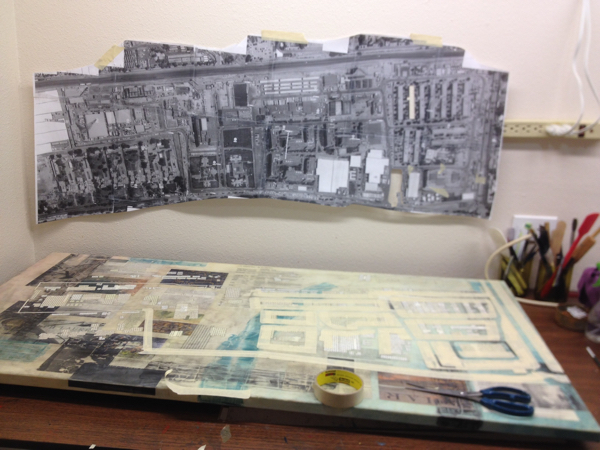 Adding layers of paint and charcoal in collage painting sitting on a work table with google maps image on wall behind it.