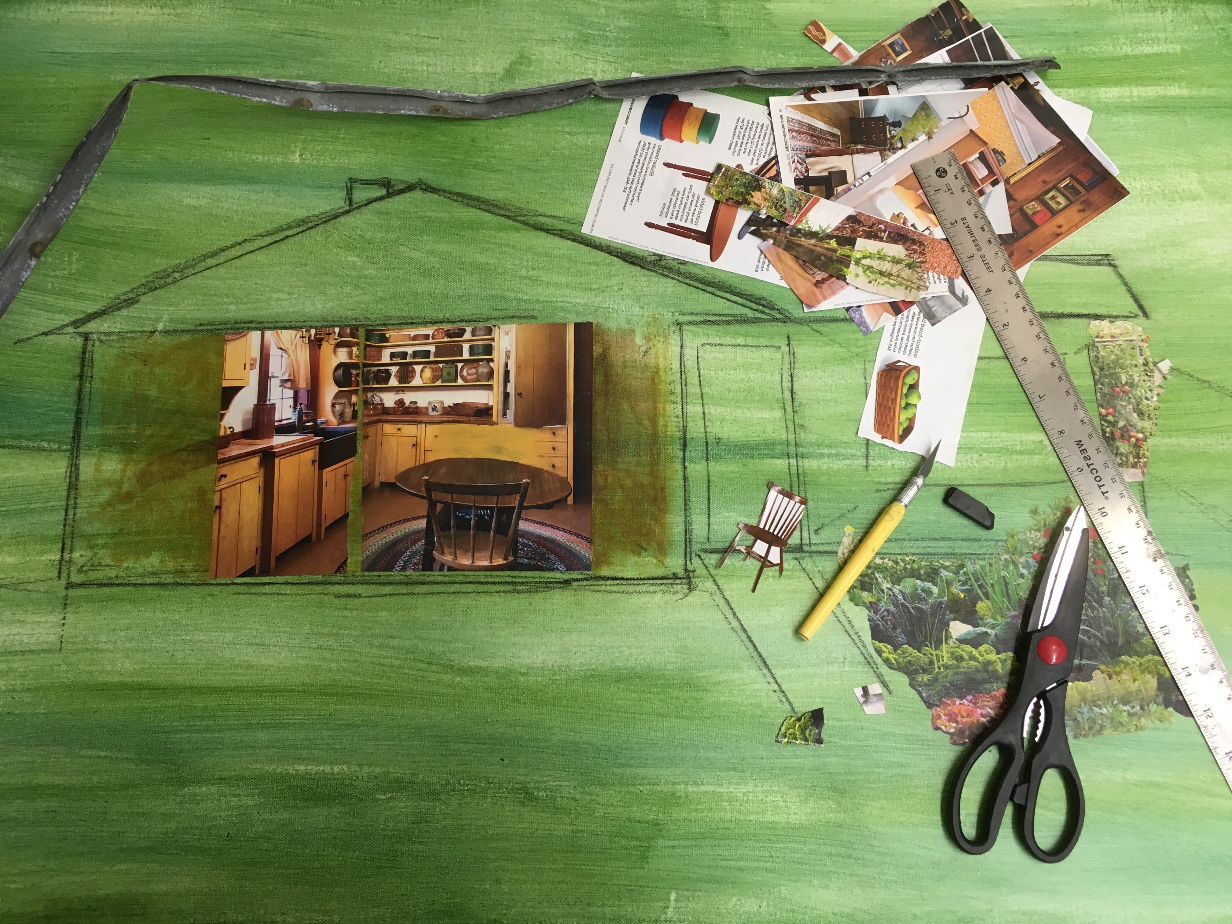 Collage painting in progress house drawn in green canvas with magazine clippings, scissors, and ruler.