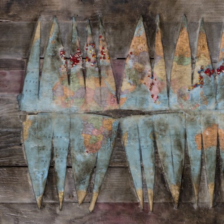 Encaustic painting made with cut up globe and map push pins.