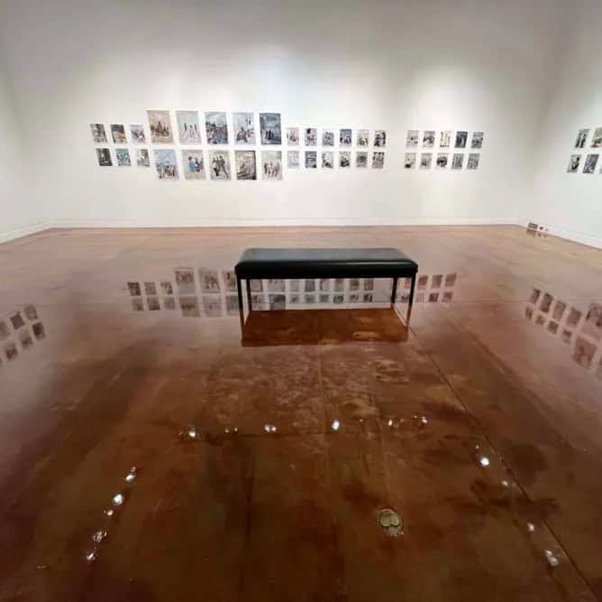 Gallery installation of the exhibit When the World Looks Away, artwork hung on the wall with reflections of art in the polished cement floor, surrounding a bench.